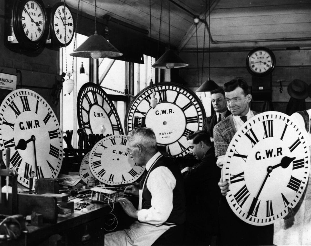 Workers surrounded by giant clock faces in a historic clock workshop